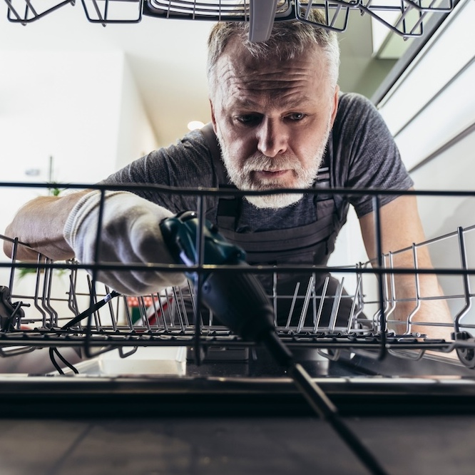 Plumber repairing dishwasher with tools.
