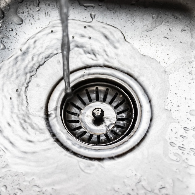 Water flowing down a drain in a stainless steel sink.