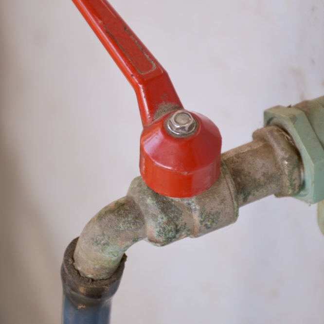 Outdoor spigot with red valve.
